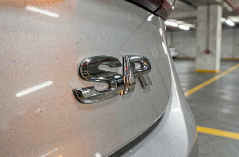 Sigle SR en chrome sur le coffre d'une berline moderne dans un parking, vue rapprochée du badge constructeur
